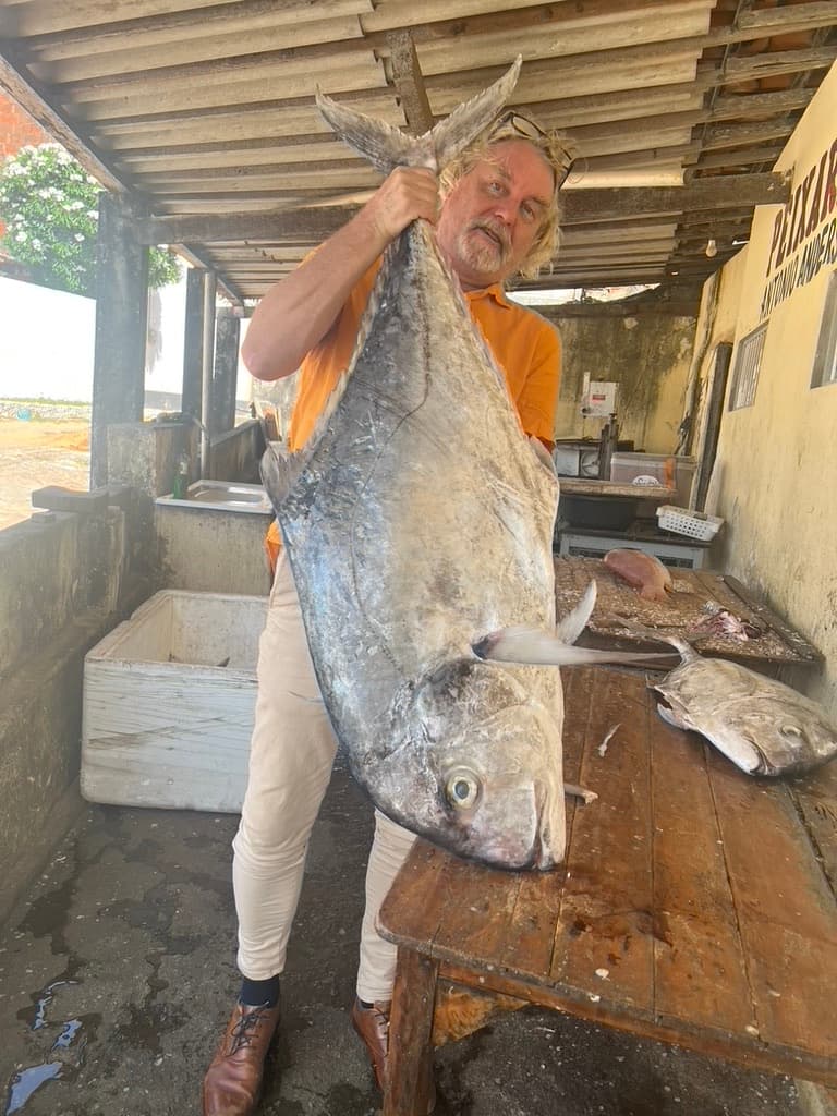 Pescador segurando um grande peixe dentro de uma estrutura rústica na vila de Emboaca