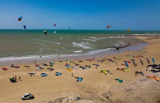 Vela de kitesurf colorida estendida na areia da praia de Emboaca, com kiters sobre o mar